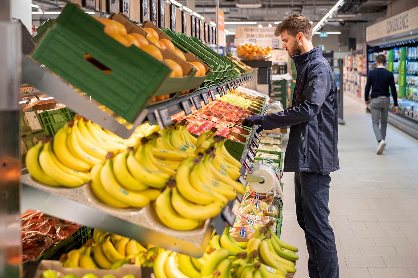 Lidl Mitarbeiter steht vor Früchteregal.