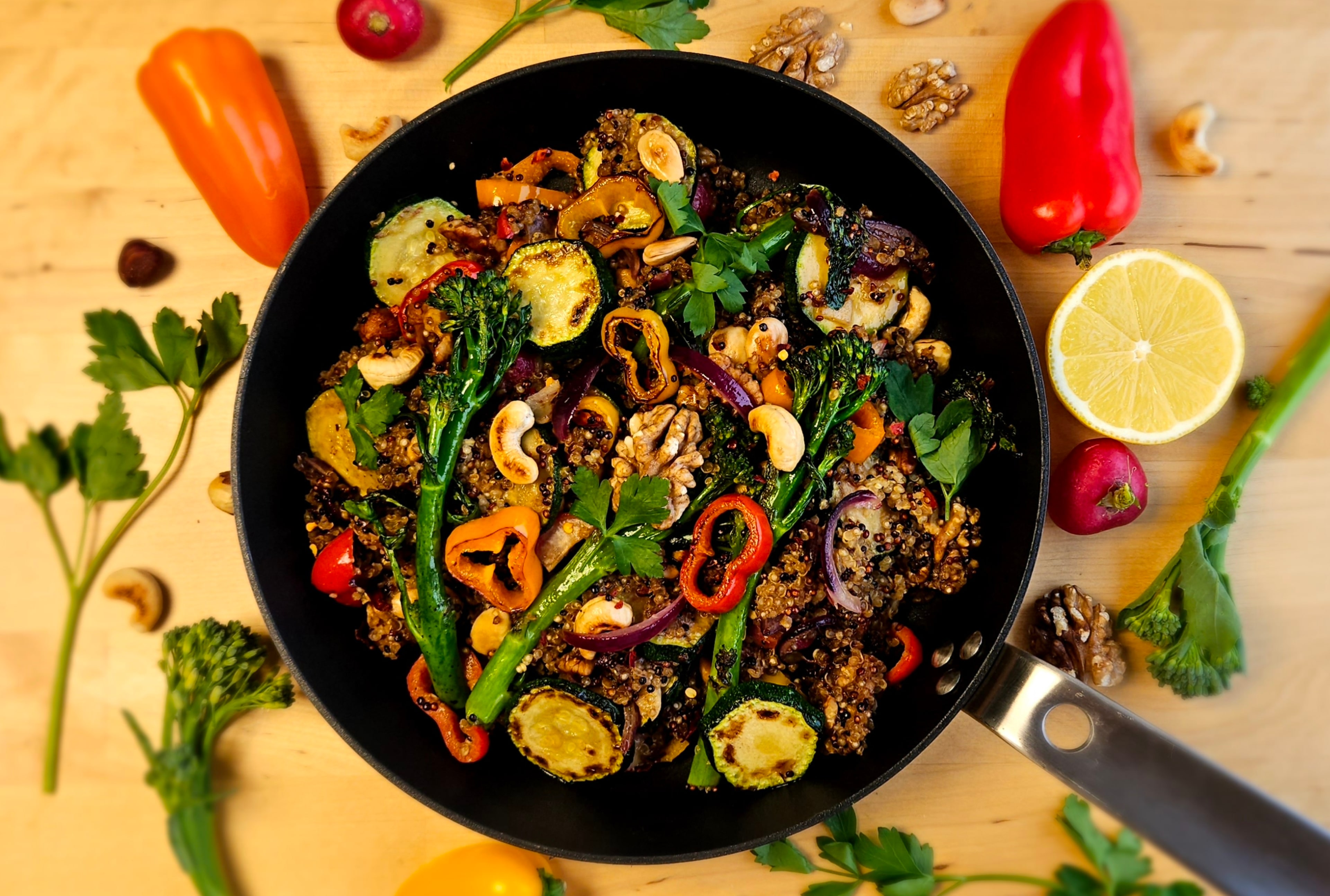 Poêlée de quinoa complet colorée avec courgettes grillées, brocolis, poivrons et noix de cajou dans une poêle noire sur fond de bois.