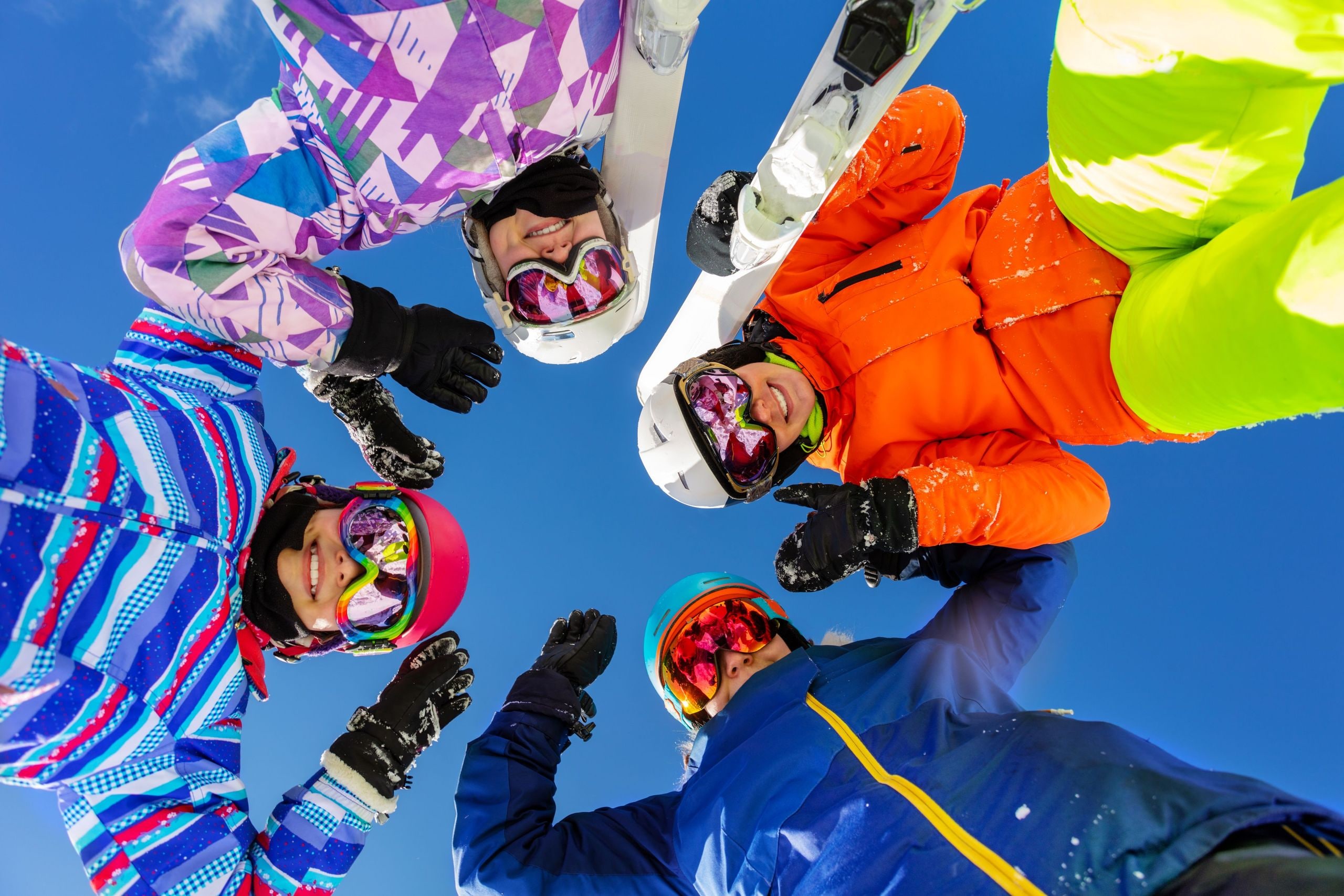 Vier Skifahrer im Kreis schauen von oben in die Kamera vor blauem Himmel.