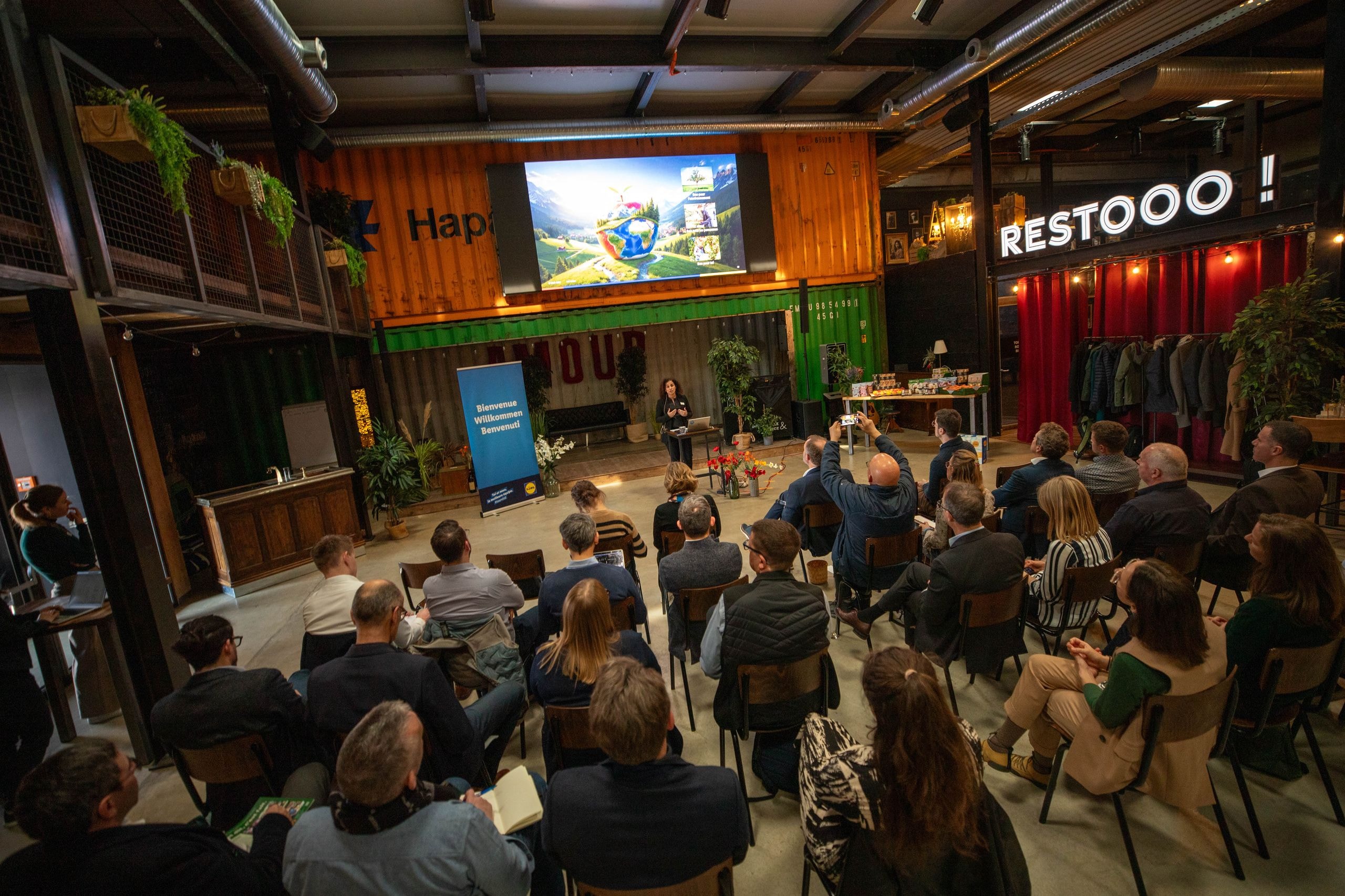 Gesamtansicht des Veranstaltungsraums mit rund 40 Teilnehmenden, die einer Präsentation zum Thema Nachhaltigkeit folgen.