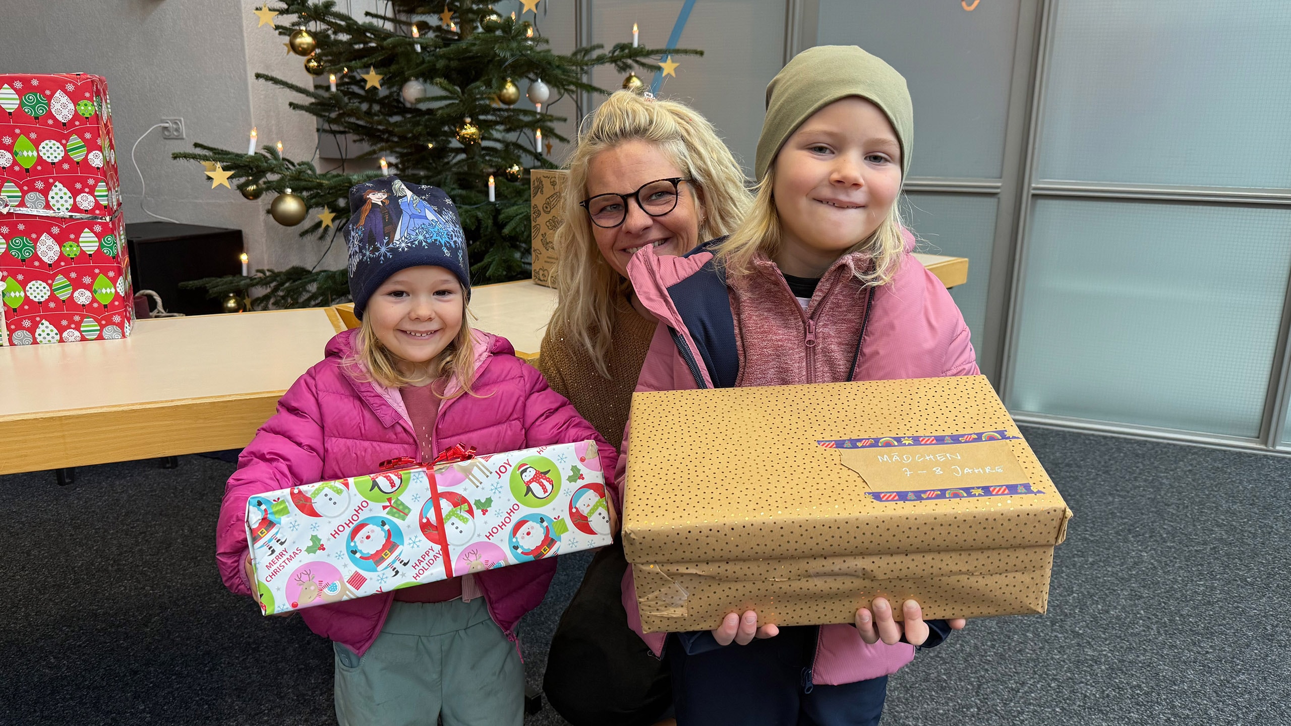 Anita Eichenberger mit zwei Kindern, die Weihnachtsgeschenke in den Händen halten.