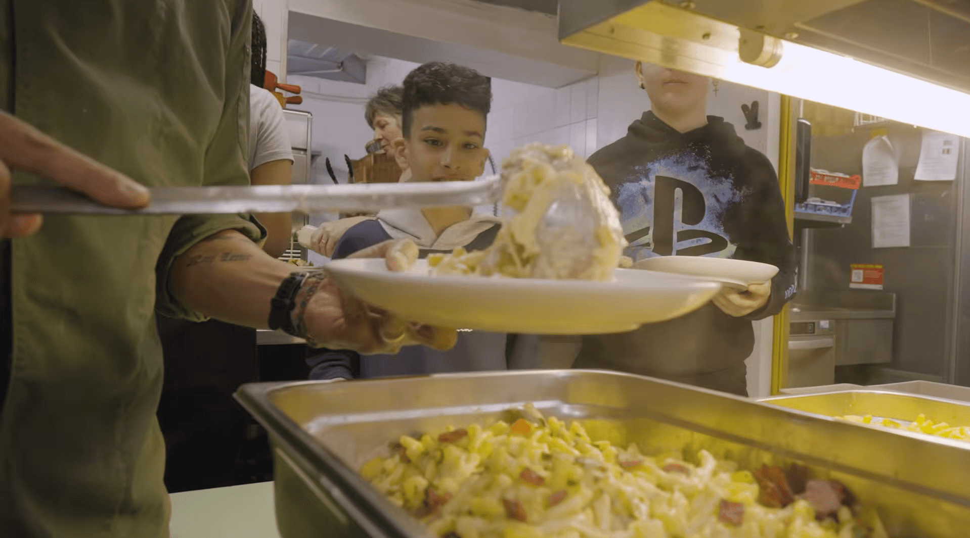 Ein Koch serviert Essen an Jugendliche in einer Kantine.