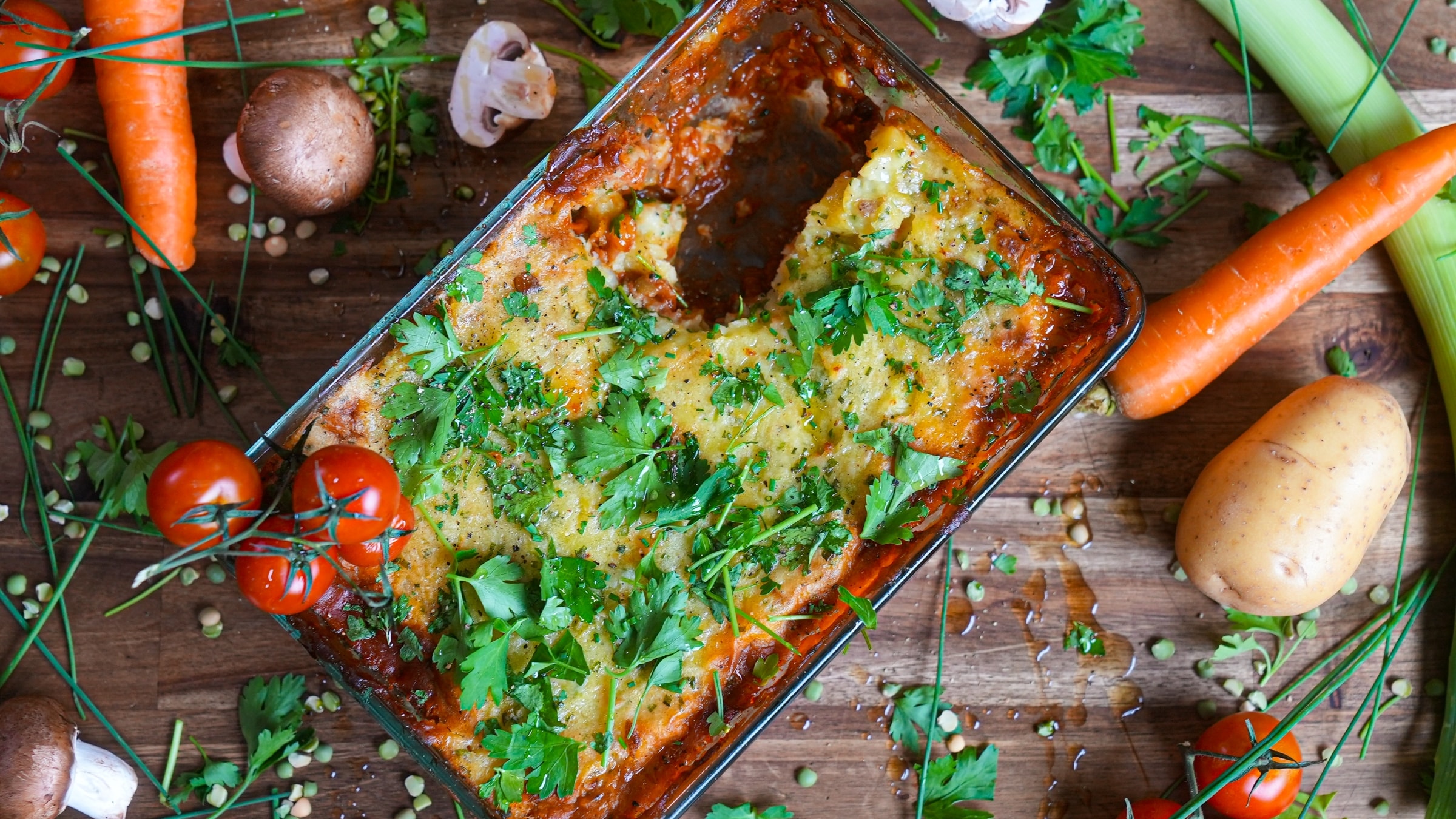 Shepherd's pie fresca in una pirofila, guarnita con prezzemolo e circondata da verdure crude su fondo di legno.