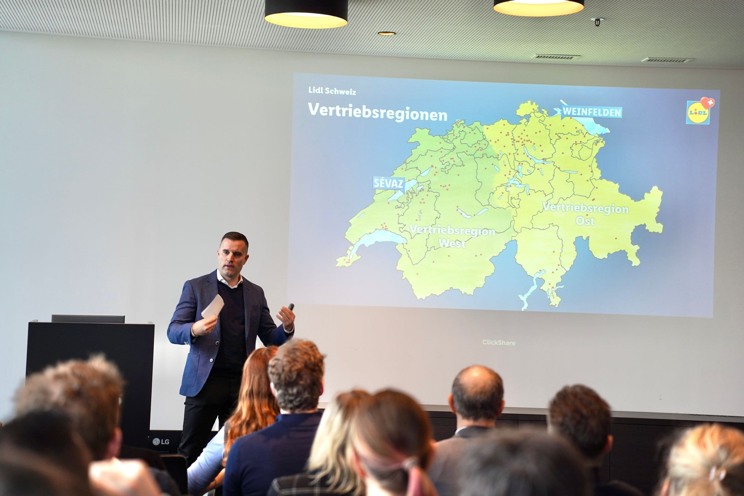 e CEO de Lidl Suisse Nicholas Pennanen explique les régions de distribution nationales à l'aide d'une carte de la Suisse devant l'auditoire des parties prenantes.