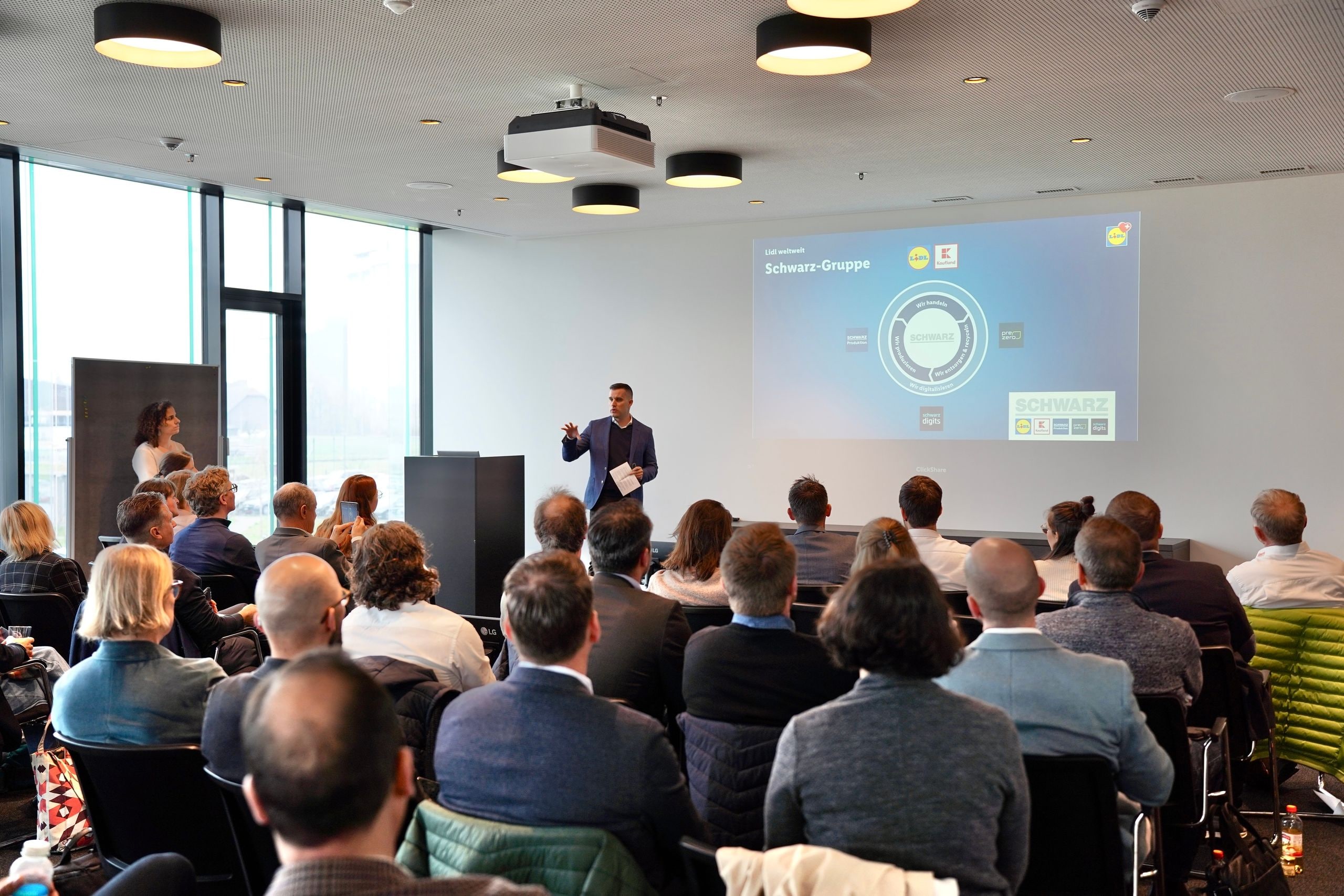 Dipendenti Lidl presentano iniziative CSR a un gruppo di persone in un contesto evento professionale.
