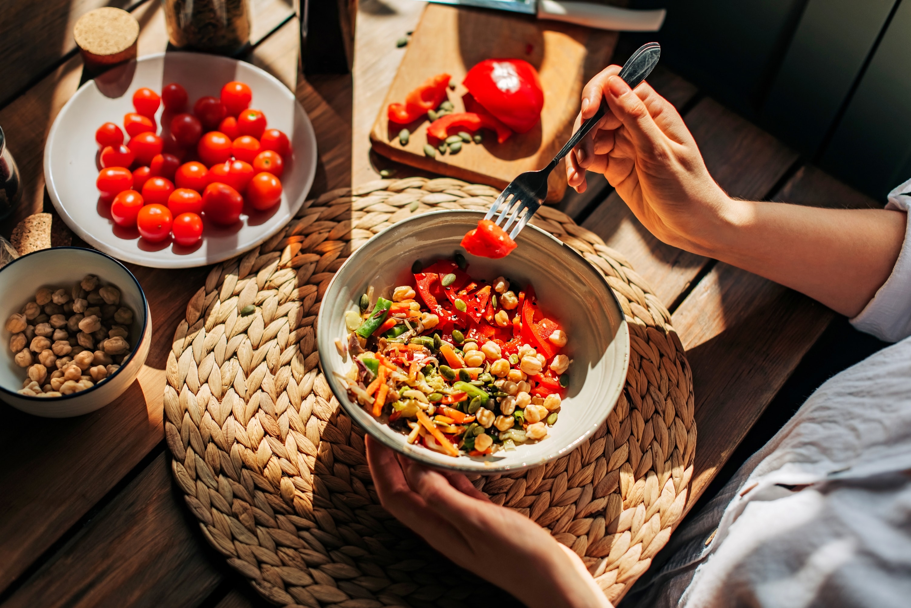 Eine Schüssel mit einem frischen Salat aus Kichererbsen, Paprika und Kernen auf einem Holztisch.