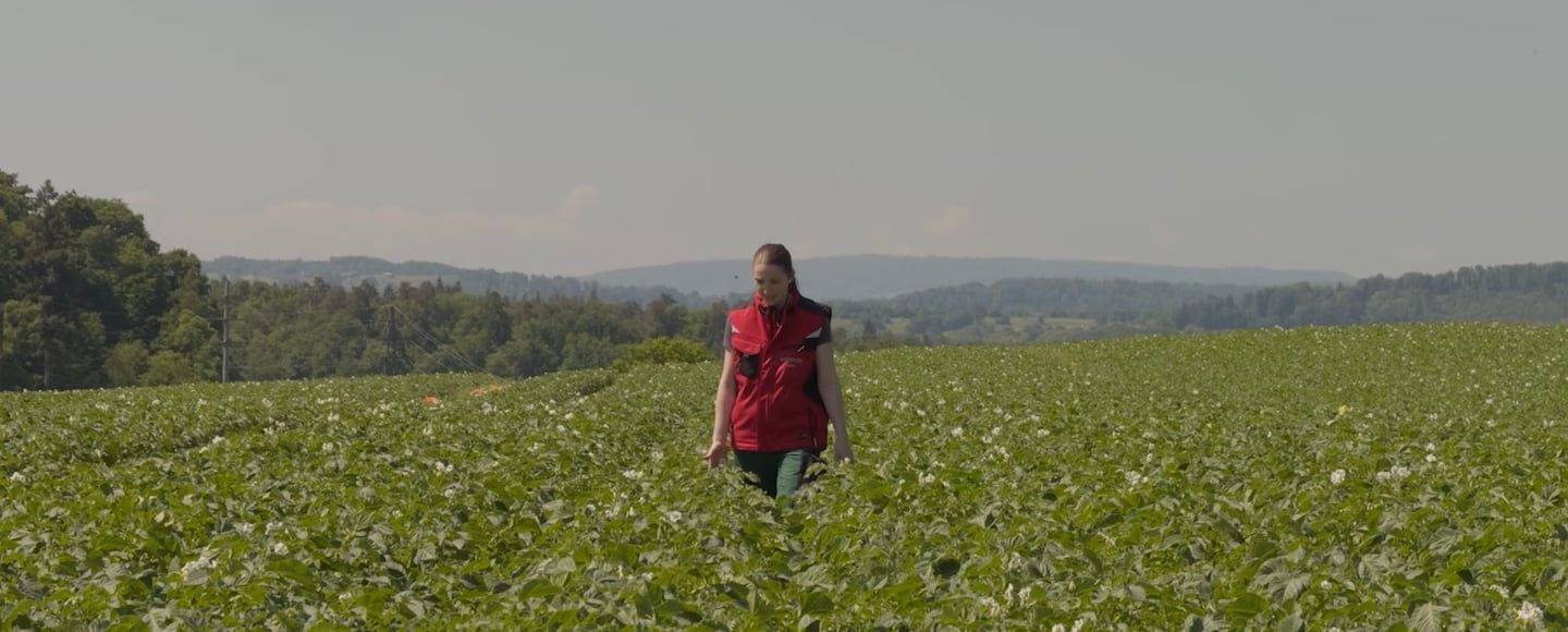 Vorschaubild für das Video, zeigt eine Frau mit roter Jacke im Feld stehend.